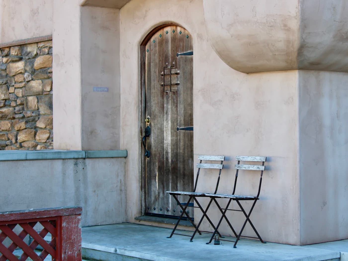Two folding metal chairs set outside an arched wooden door in a pale plaster wall.